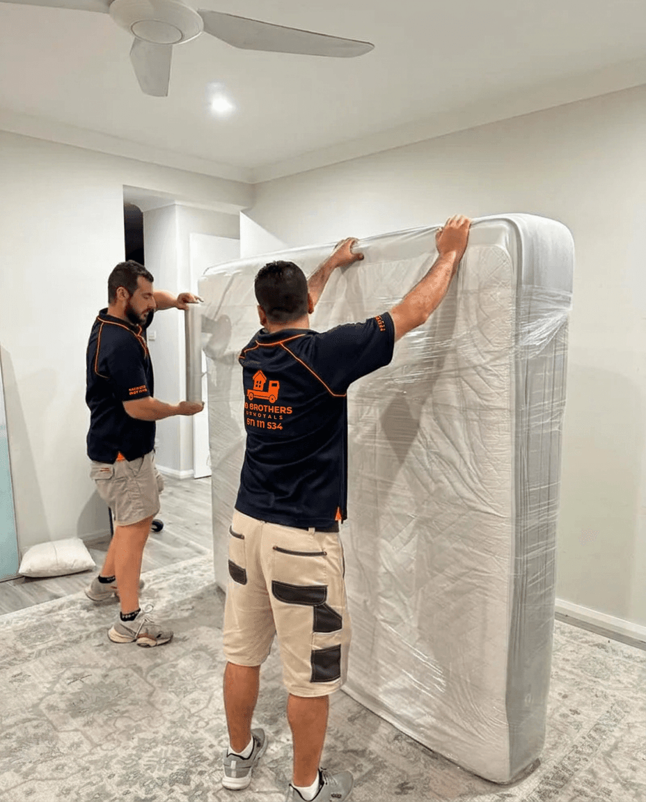 Two removalists wrapping a mattress in heavy-duty protective plastic before moving